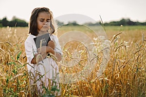 Girl holds bible in her hands. Reading the Holy Bible in a field. Concept for faith, spirituality and religion.