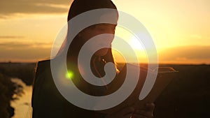 A girl holds Bible in his hands and studies the word of God at sunrise on top of mountain. A woman reads a book in rays