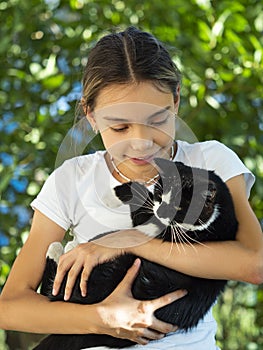 The girl holds a black stray cat in her arms and looks at him.