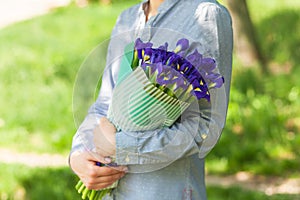 Girl holds a bouquet with irises, on a background of green grass