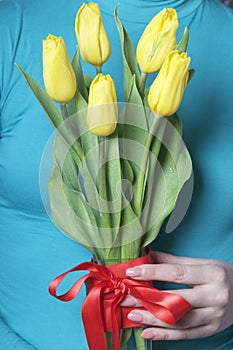 The girl holds a bouquet of yellow tulips. Flowers in a glass vase wrapped in red ribbon, tied to a bow.