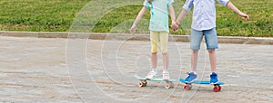 The girl holds the boy`s hand, they together skateboard in the city park in the summer