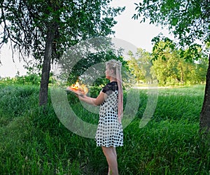 Girl holds a burning book in her hands. A young woman in a forest burns a book
