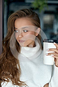 Girl holds cup of coffee. Beautiful young woman drinking cappuccino.