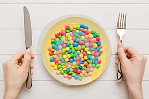 the girl holds cutlery in her hands and eats sweets in a plate. Health and obesity concept, top view on colored