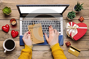 Girl holds debit card, laptop, chooses gifts, makes purchases, cup of coffee, two hearts, succulents on wooden table