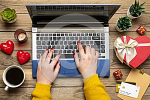 Girl holds debit card, laptop, chooses gifts, makes purchases, cup of coffee, two hearts, succulents on wooden table