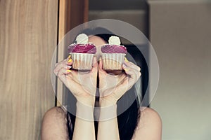 The girl holds delicious cupcakes with white cream in her hands, decorated with balls sprinkled with coconut powder and closes her