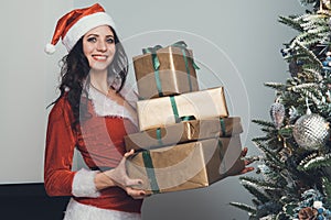 Girl holds four gifts in a gold wrapper in an apartment decorated for the new year. Young woman in red Santa Claus costume pulls