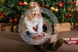 A girl holds a gift box with a Christmas gift on the background of a Christmas tree.