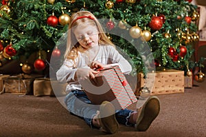 A girl holds a gift box with a Christmas gift on the background of a Christmas tree.