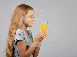 A girl holds a glass of juice in her hands with two hands, profile view