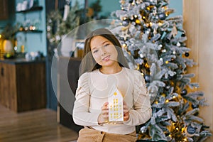 Girl holds a glowing toy house in her hands to decorate the house for Christmas and New year in anticipation of a fairy tale