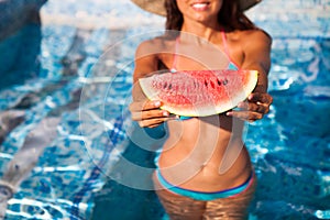 A girl holds half a red watermelon over a blue pool, relaxing o