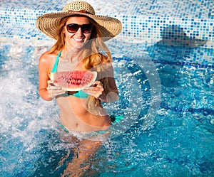 A girl holds half a red watermelon over a blue pool, relaxing o