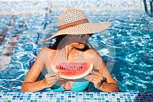 A girl holds half a red watermelon over a blue pool, relaxing o