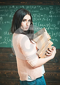 Girl holds heavy pile of old books, chalkboard background. Diligent student preparing for exam test. Profound research