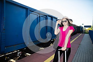 The girl holds her big hat so that the blast from the freight train ahead does not break it.