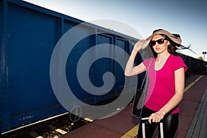 The girl holds her big hat so that the blast from the freight train ahead does not break it.