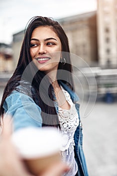 Girl holds her hand with a glass of coffee to go.Beautiful girl with an elegant hairstyle laughs while walking down the street