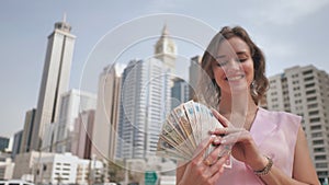 The girl holds in her hands the money of the United Arab Emirates on the background of the city center of Dubai.