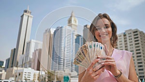 The girl holds in her hands the money of the United Arab Emirates on the background of the city center of Dubai.