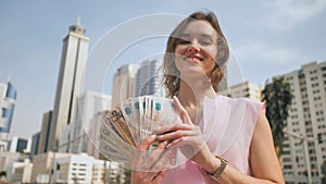 The girl holds in her hands the money of the United Arab Emirates on the background of the city center of Dubai.