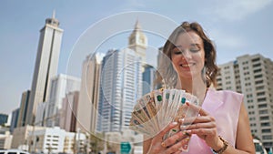 The girl holds in her hands the money of the United Arab Emirates on the background of the city center of Dubai.
