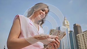 The girl holds in her hands the money of the United Arab Emirates on the background of the city center of Dubai.