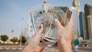 The girl holds in her hands the money of the United Arab Emirates on the background of the city center of Dubai.