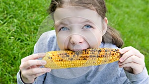 Girl holds in her hands a roasted corn cob and bites her teeth