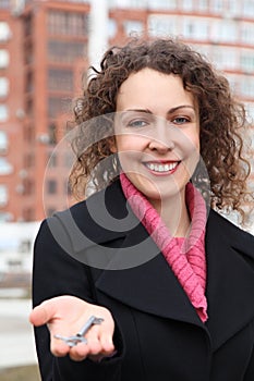 Girl holds key on palm against many-storeyed house