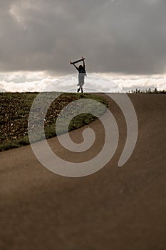 girl holds longboard aloft beneath overcast skies.