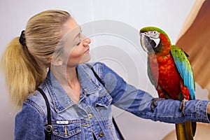 A girl holds a Macaw parrot on her hand and looks at him with a smile in a contact zoo, where you can touch animals and make a pho