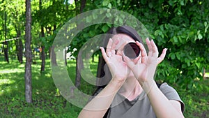 The girl holds an ND filter in her hands and looks through it with one eye and slowly twists it, the filter turns black