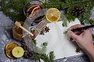 The girl holds a pen in her hands over a blank page of a notebook next to mulled wine, spices, anise,