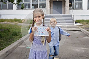 Girl holds picture with back to school message and boy with backpack runs after first offline day