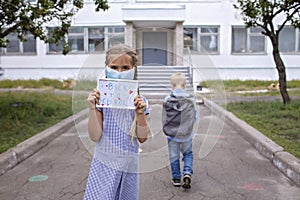 Girl holds picture with back to school message and boy goes to school after first offline day