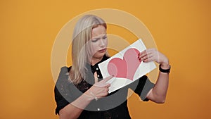 Girl holds a piece of paper with a red heart and touches her tongue with finger