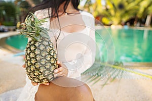 Girl holds pineapple in hands on the background of the pool in the tropics