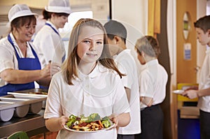 Girl holds a plate of food in school cafeteria, head turned photo