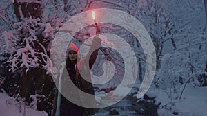 The girl holds a red burning signal light in her hand. A woman in a snowy winter forest, trees