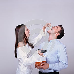 Girl holds the remote control from the TV and spills popcorn into the guy`s mouth
