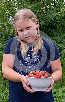 The girl holds a ripe juicy red fragrant strawberry in her hands.