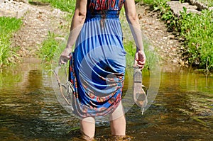 Girl holds sandals wade barefoot flowing stream