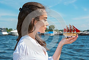 Girl holds a small ship with red sails. Modern Assol.