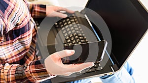 girl holds smartphone and laptop in hands, selective focus on the hand