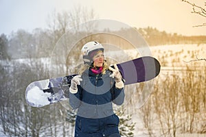 The girl holds a snowboard in her hands, she is dressed in a mountain jacket and a helmet