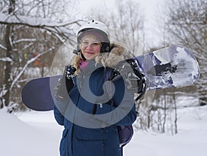 The girl holds a snowboard in her hands, she is dressed in a mountain jacket and a helmet