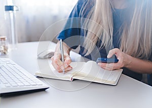 Girl holds a spartphone in her hand and takes notes in her notebook